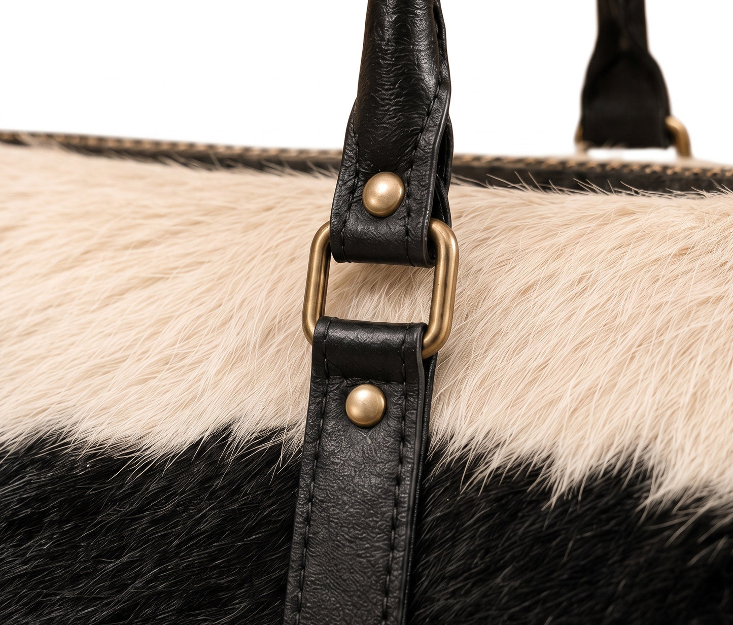 Close-up of a handbag featuring a black and cream cowhide pattern with a black leather strap and brass-tone hardware.