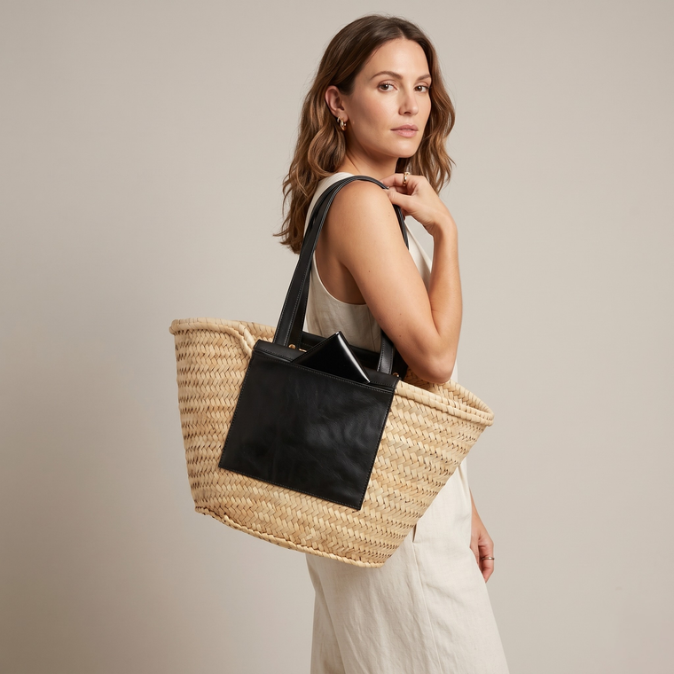 Woman holding a straw bag with black accents against a neutral background