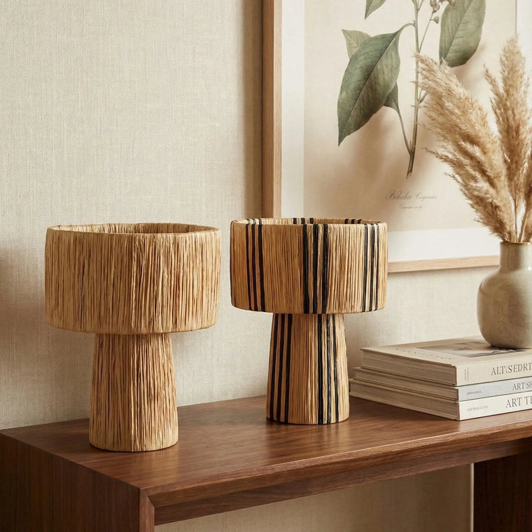 Two wooden vases on a shelf with a neutral wall and books in the background