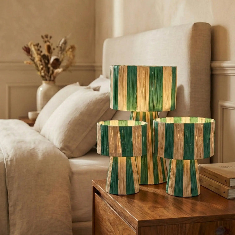 Three wooden lamps with green and beige stripes on a nightstand next to a bed.