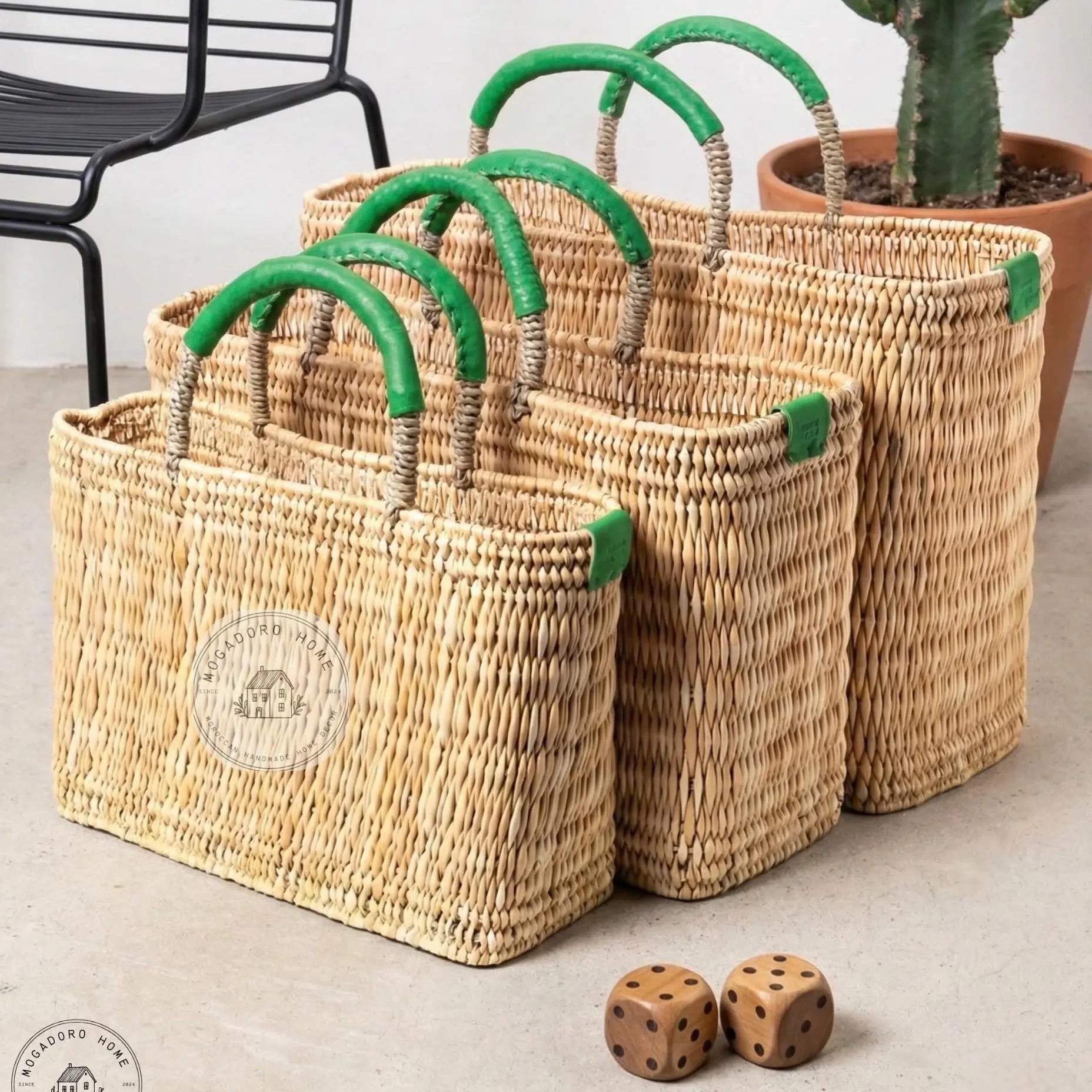 Set of woven baskets with green handles on a light surface, with a cactus plant in the background.