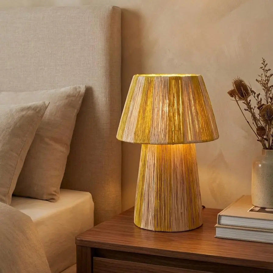 Wooden table lamp on a nightstand next to a bed with beige bedding.