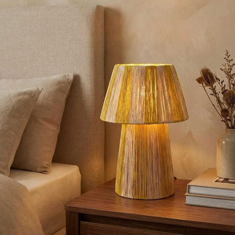 Wooden table lamp on a nightstand next to a bed with beige bedding.