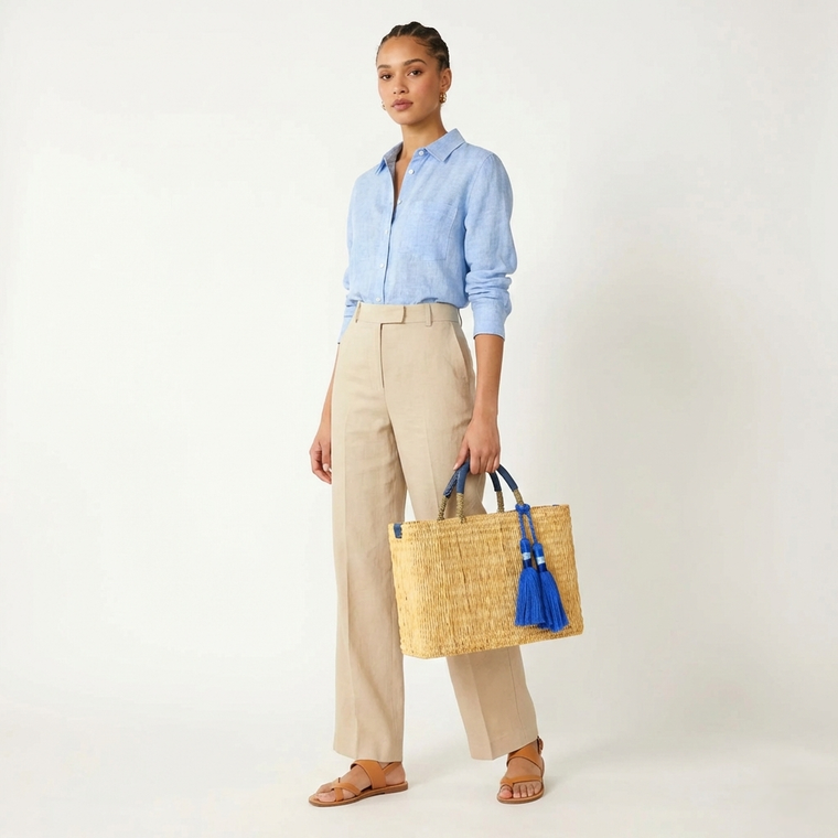 Woman holding a straw bag with blue tassels against a white background