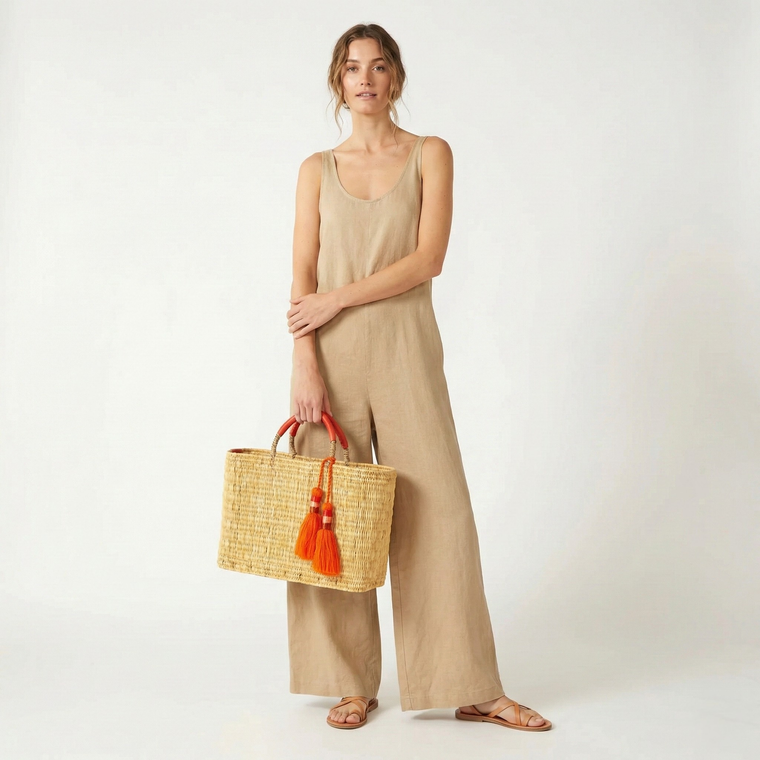 Woman holding a woven bag with orange tassels against a white background