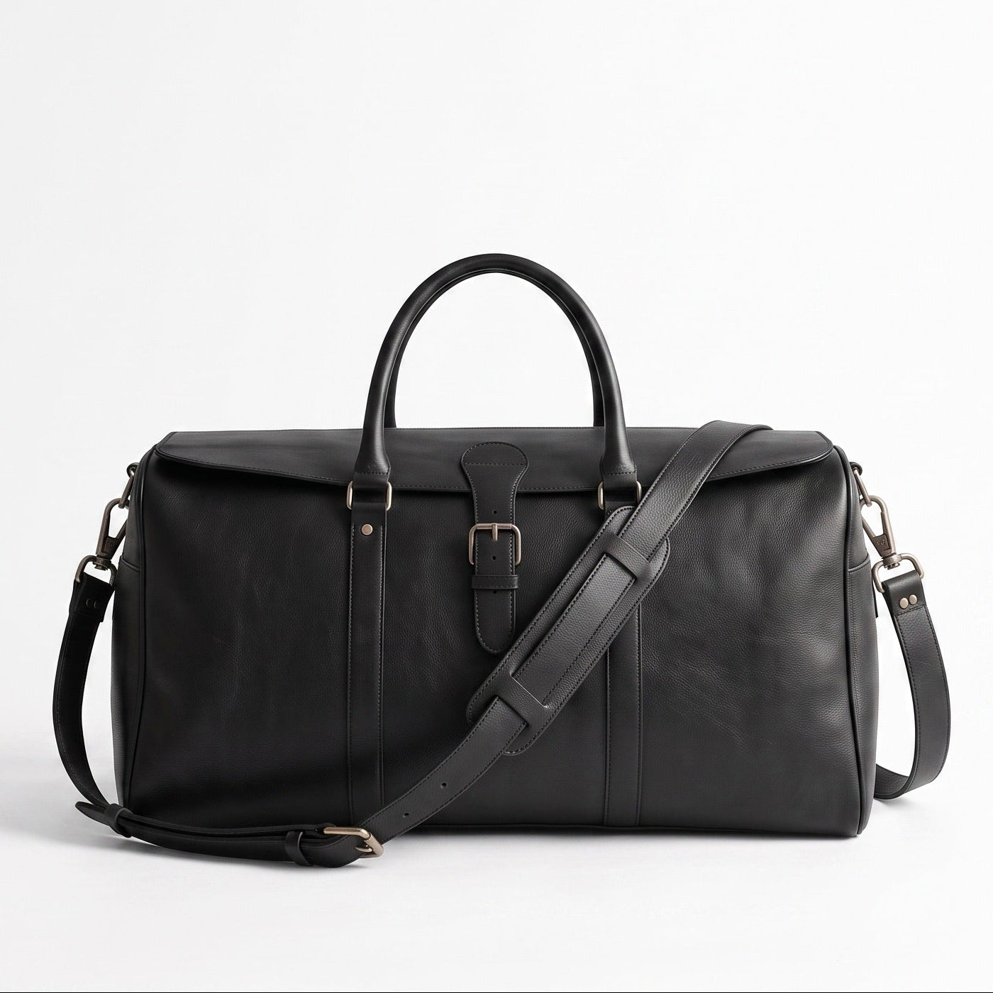 A black leather duffel bag with dual top handles, a front buckle closure, and an adjustable shoulder strap, photographed on a clean white studio background.