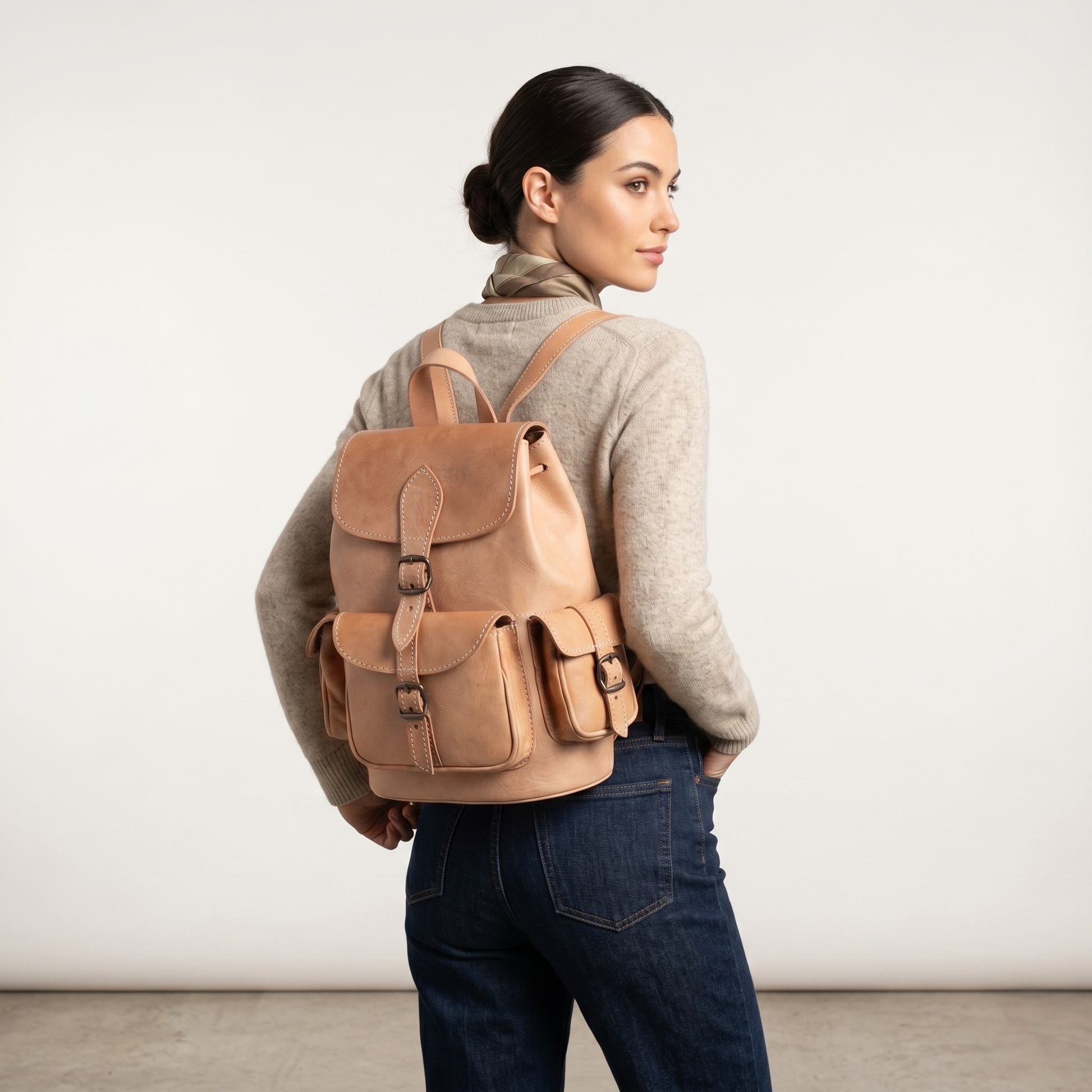 Woman wearing a brown leather backpack against a plain background