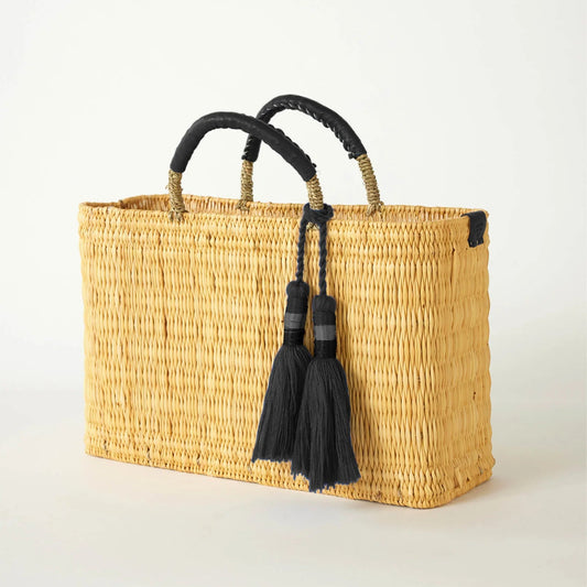 Woven basket with black handles and tassels on a light background