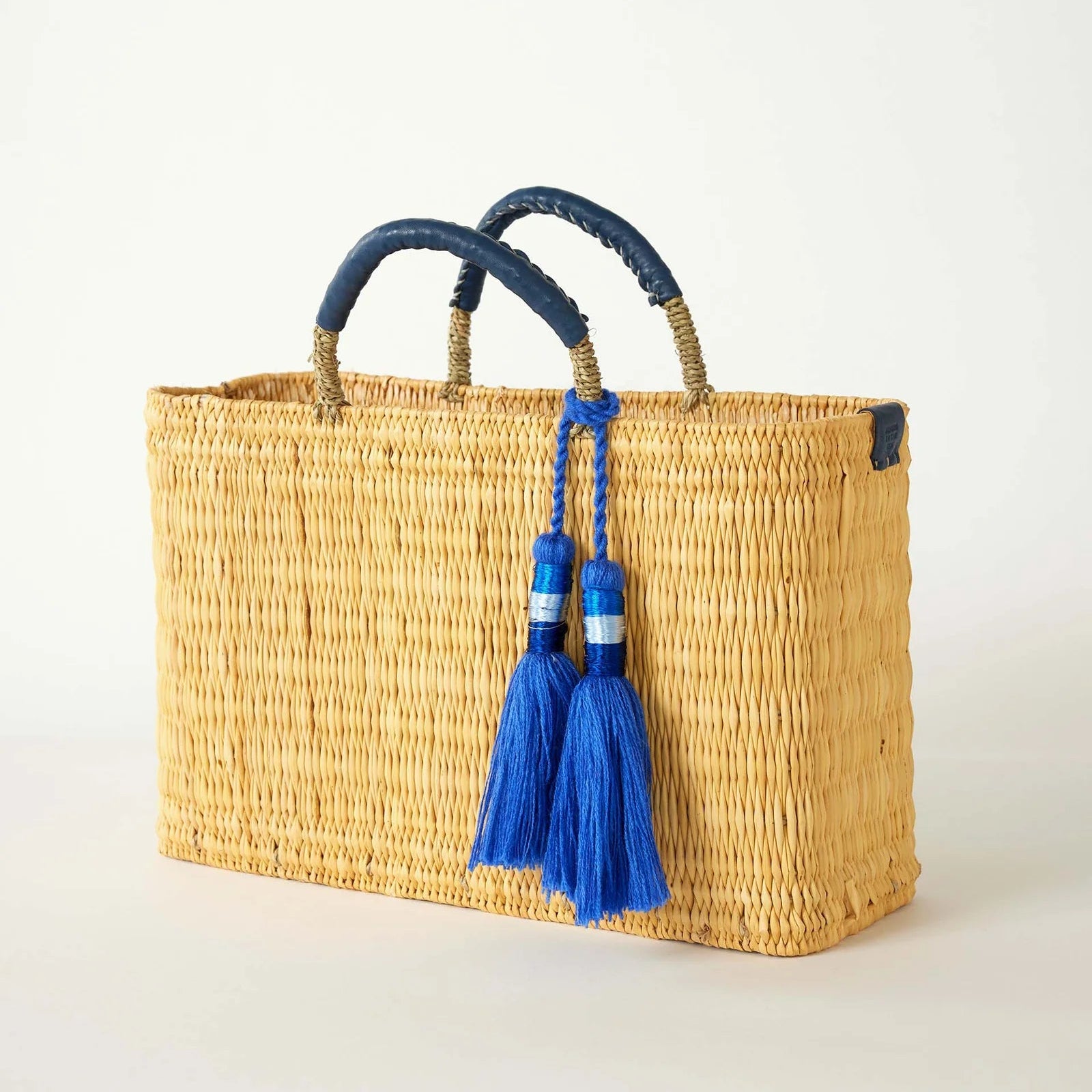 Woven basket with blue handles and tassels on a light background