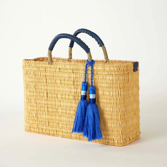 Woven basket with blue handles and tassels on a light background
