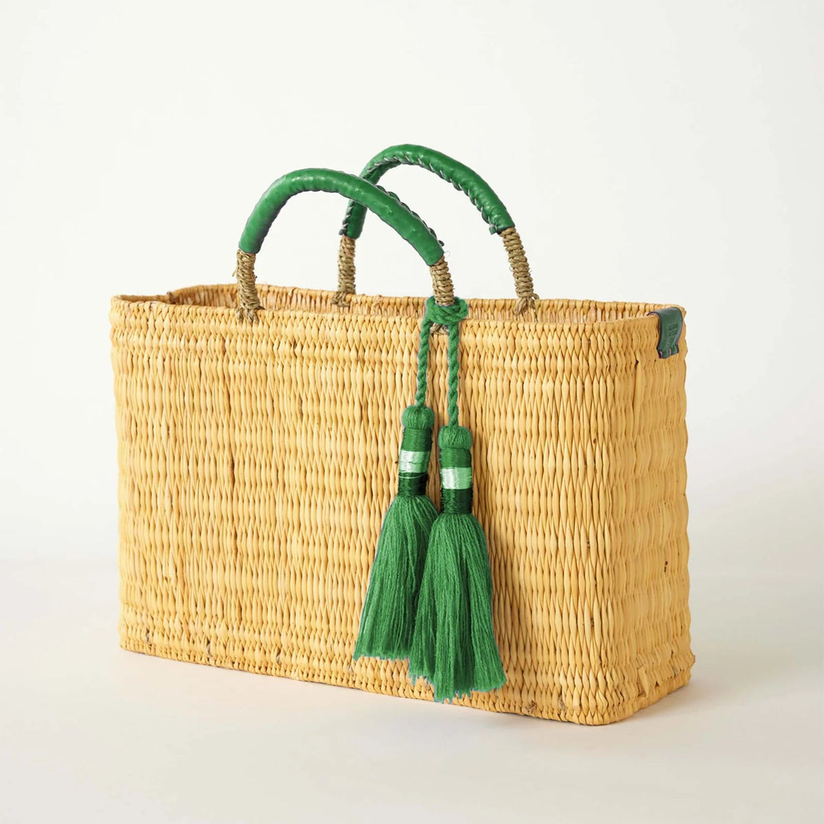 Woven basket with green handles and tassels on a white background
