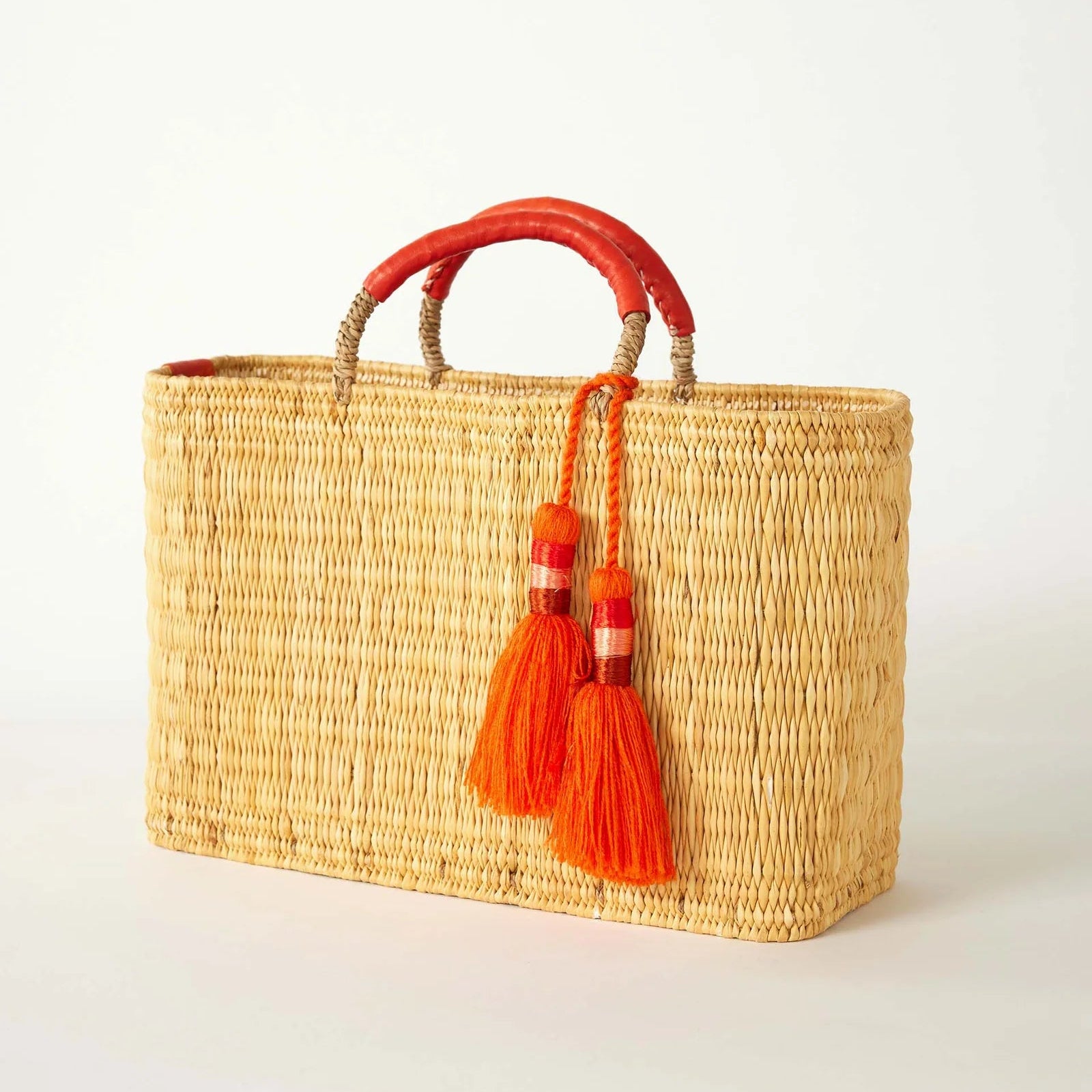 Woven handbag with orange handles and tassels on a white background 